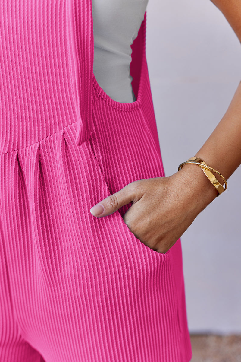 Pink ribbed knit romper with ruffled bib front and side pocket detail