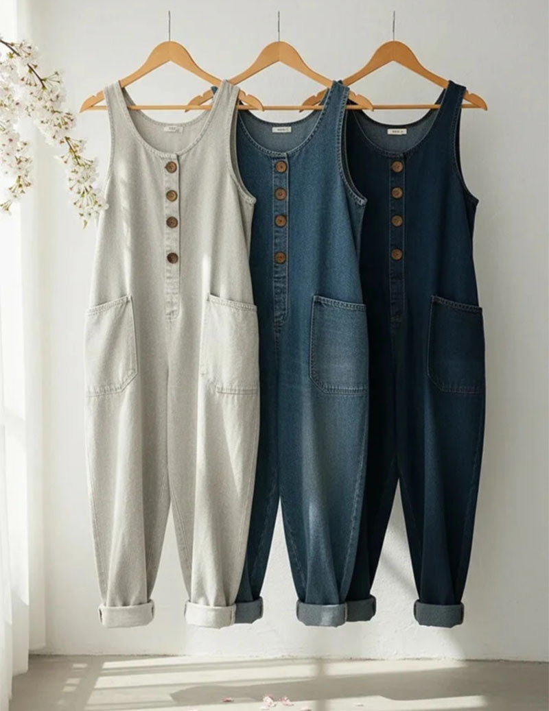 Denim sleeveless jumpsuits in white, blue, and dark denim on wooden hangers