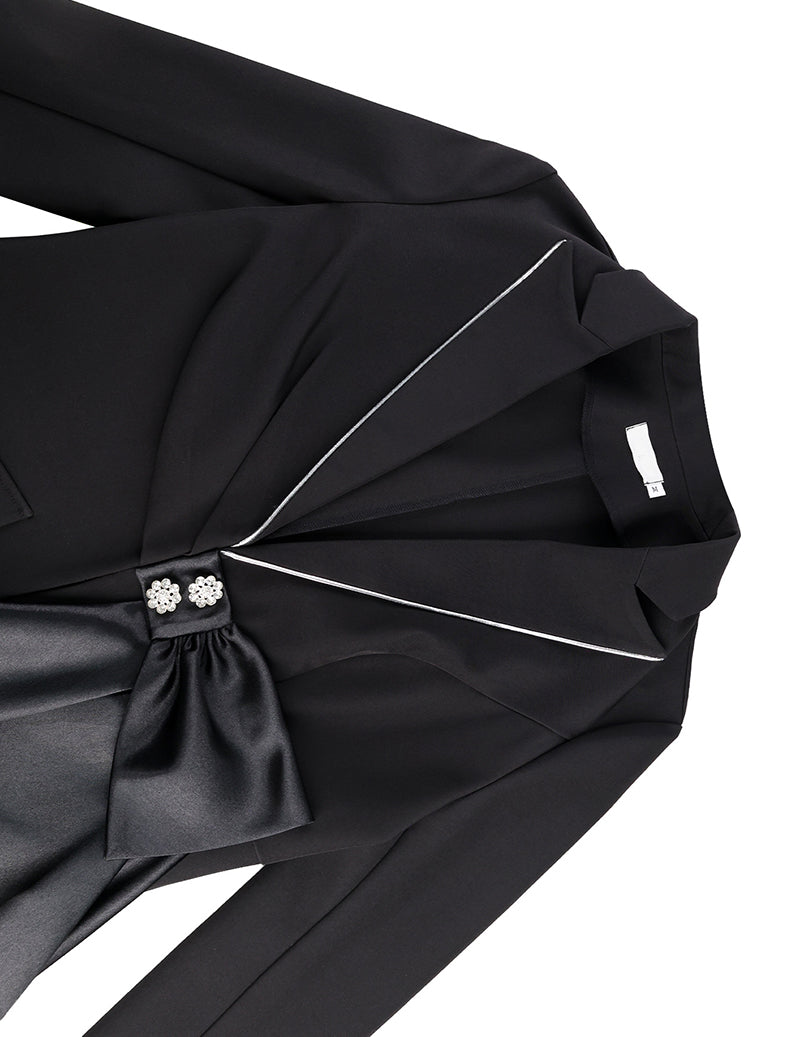 Black blazer close-up showing satin sash bow across front with contrast trim piping
