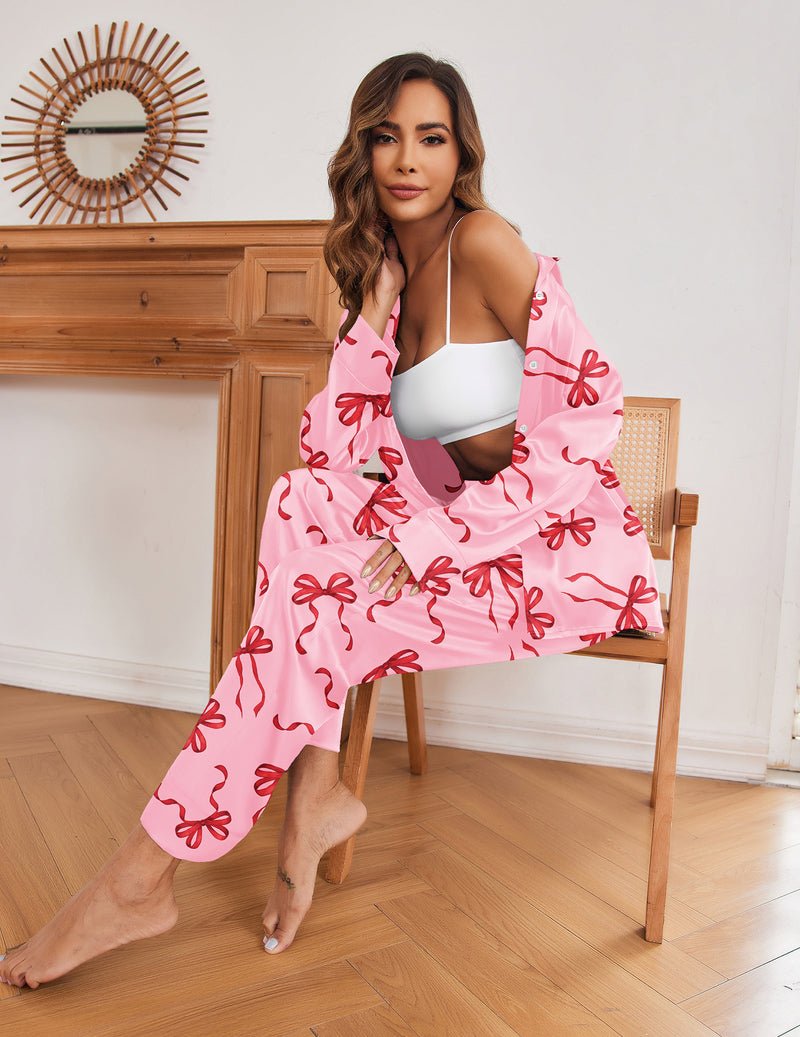 Pink silk satin long-sleeve pajama set with red bow print, button-front top and matching pants