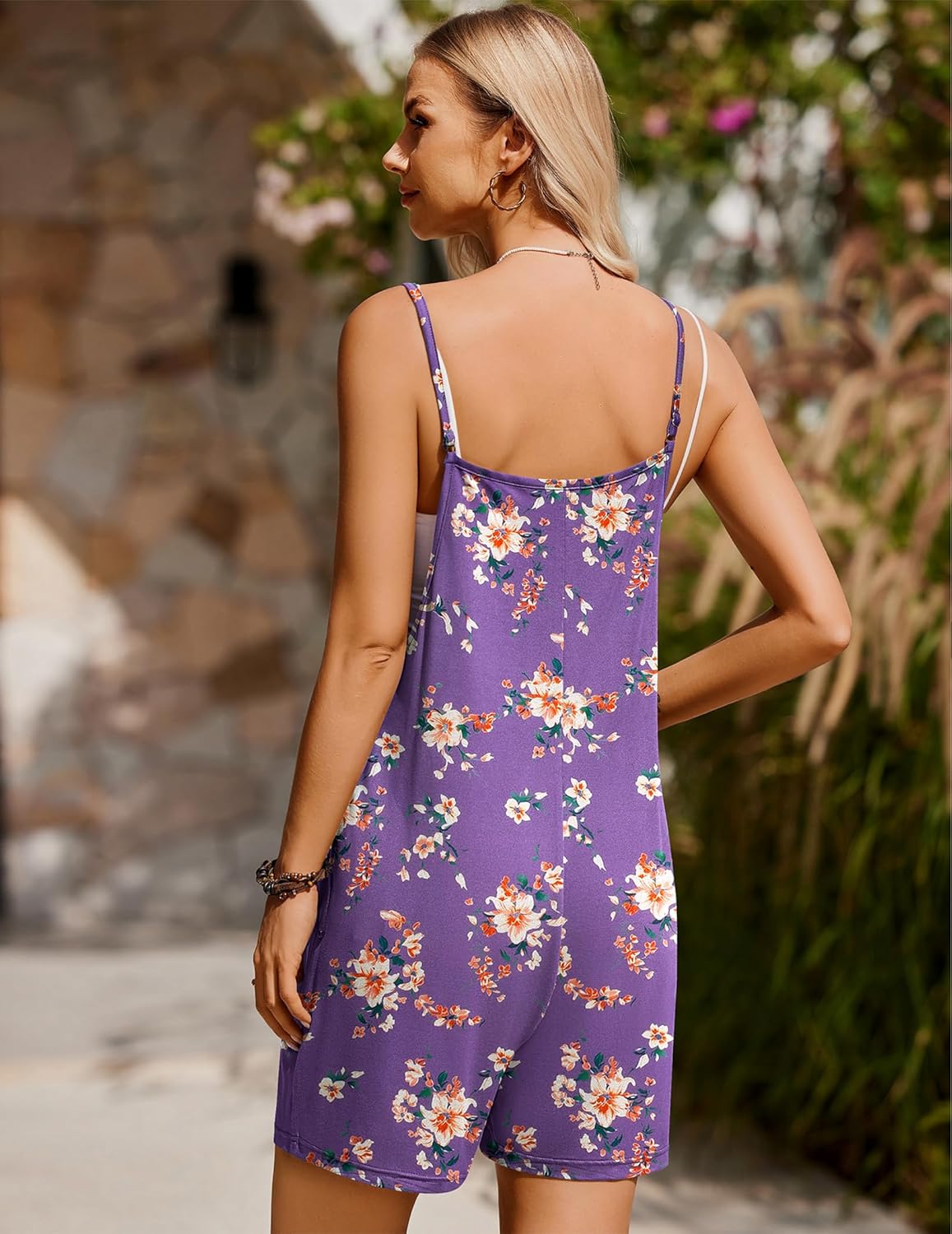 Rückansicht: ärmelloser Latzshortsanzug, violetter Grund mit buntem Blumenmuster