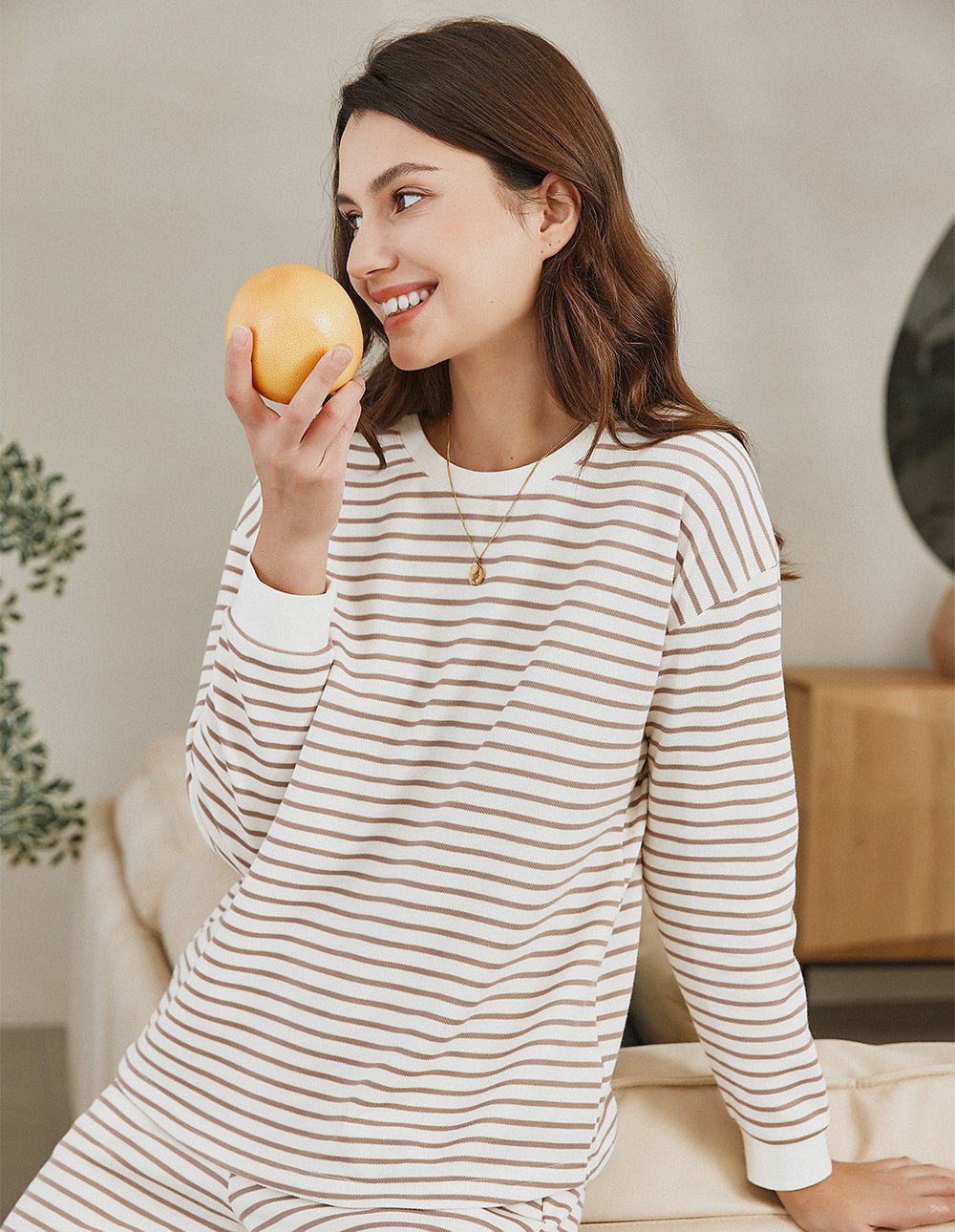 Striped cotton pajama set, long sleeves and pants, cream with tan stripes, smiling while holding orange