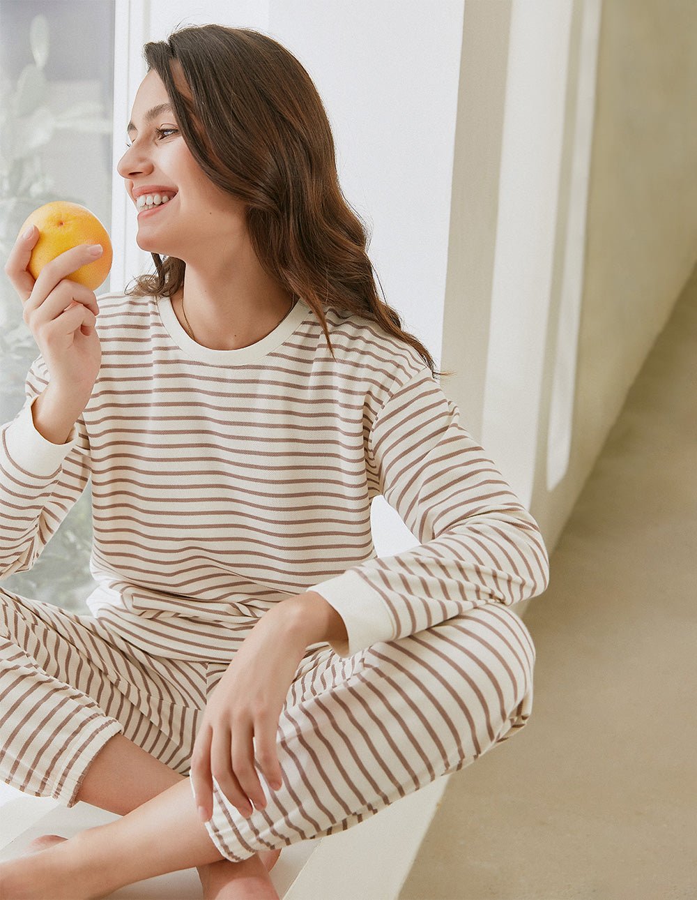 Striped cotton pajama set, long sleeves and pants, cream with tan stripes, holding orange