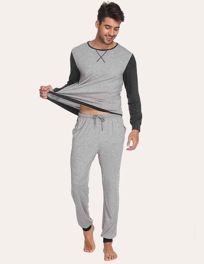 Men's two-piece pajama set with light grey top and jogger pants; holding shirt hem